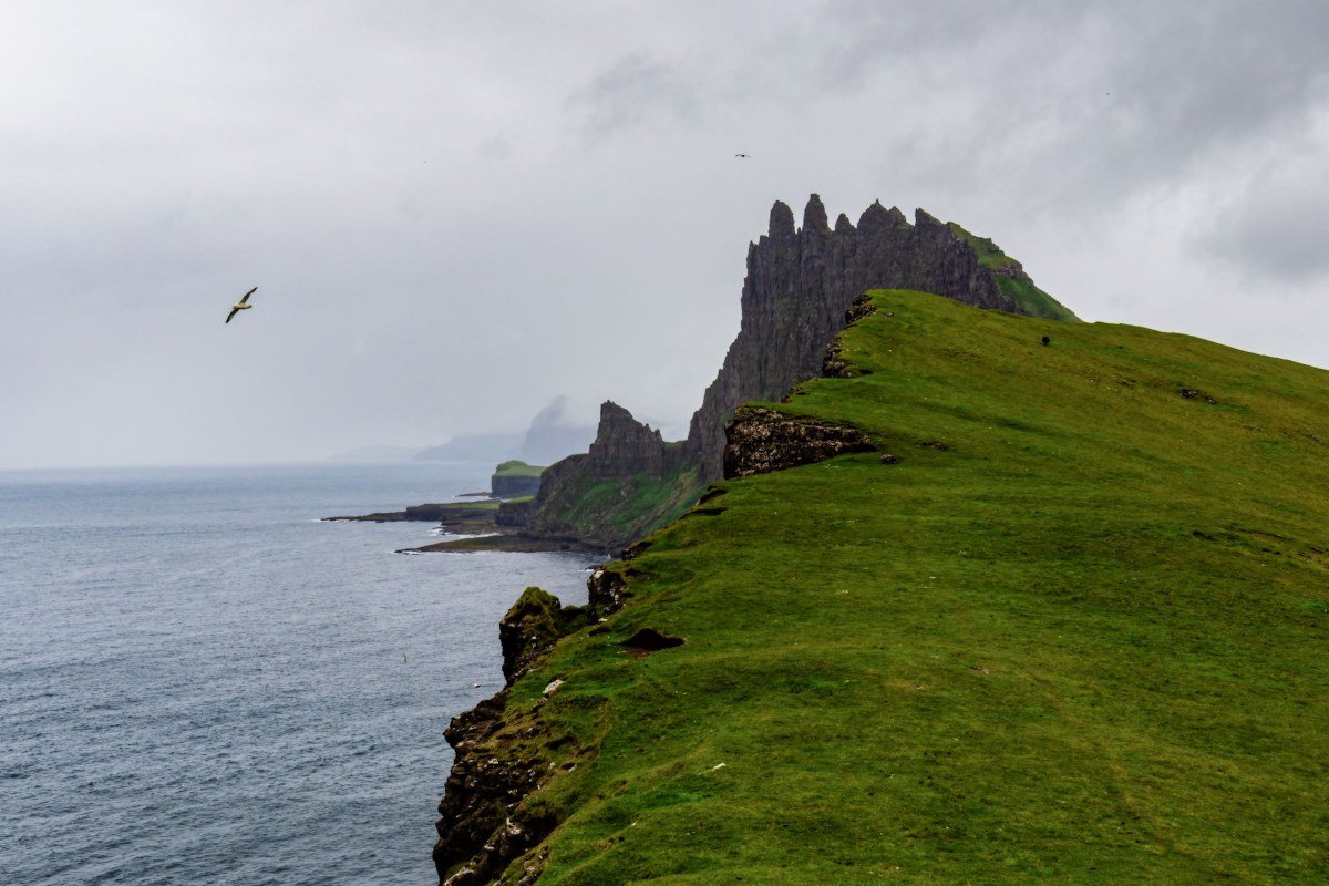 Faroe Islands dramatic sea cliffs with thick fog and green grass Sørvágsvatn lake