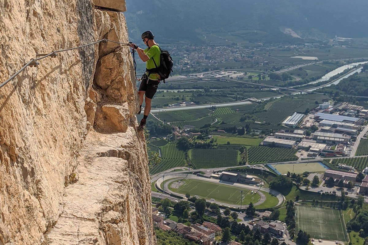 climber on iron rungs via ferrata route with jagged Dolomite peaks and orange rock face at sunrise