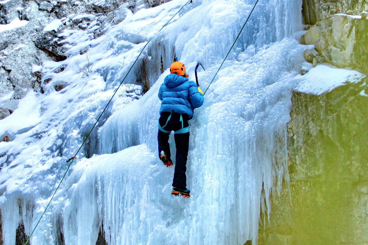 ice climber ascending frozen blue waterfall pillar in Ouray Colorado ice park surrounded by canyon walls