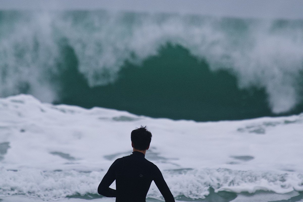 big wave surfer riding enormous Atlantic swell at Nazaré Portugal lighthouse on cliff in background