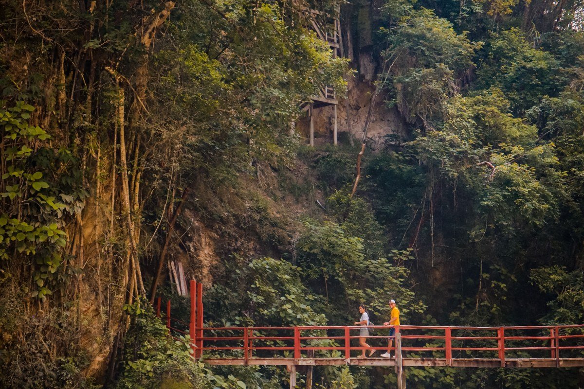 traveler jumping into turquoise limestone pool at Semuc Champey Guatemala with jungle canopy overhead