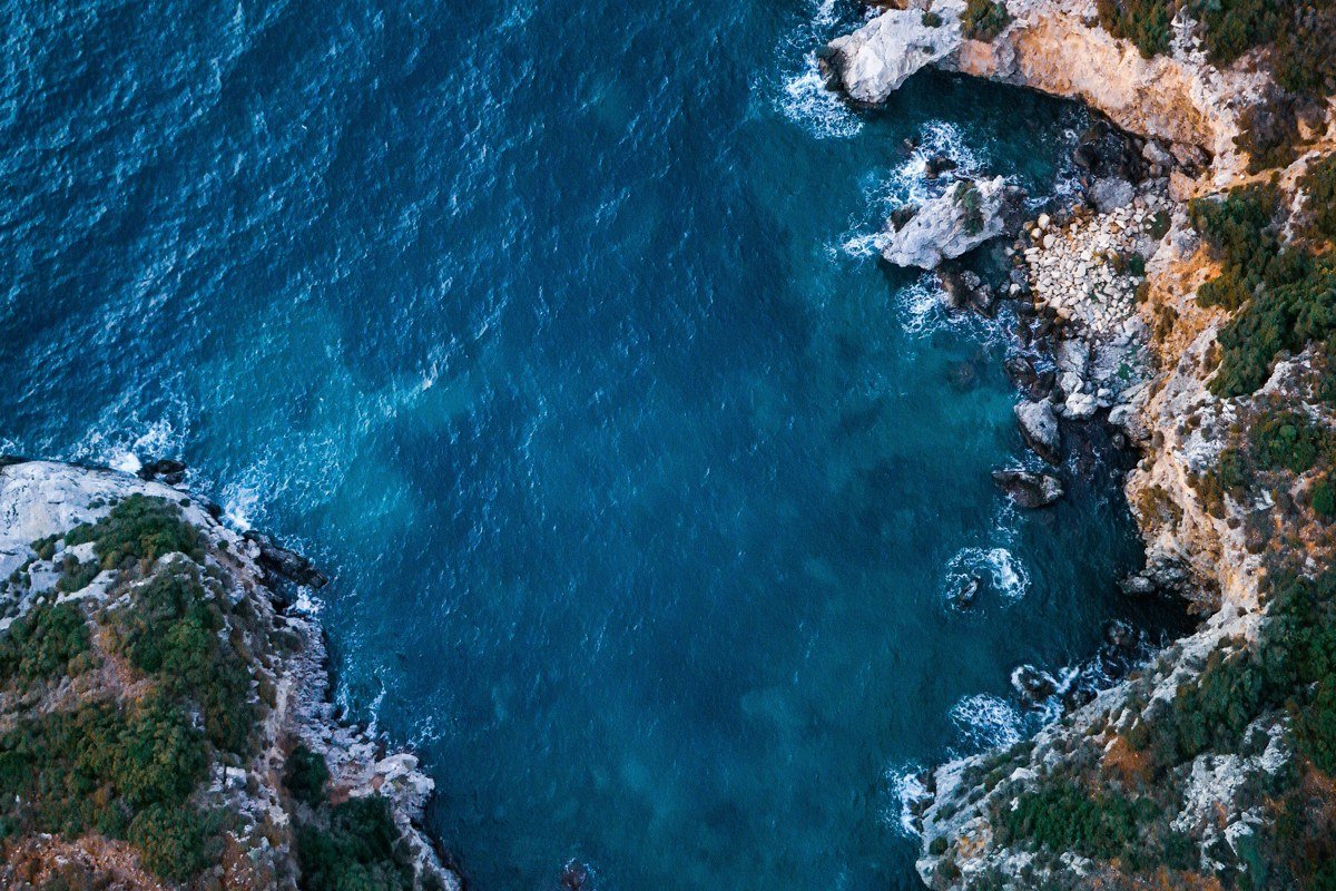 aerial view of turquoise Mediterranean cove with white-washed Greek village cliffs and olive groves