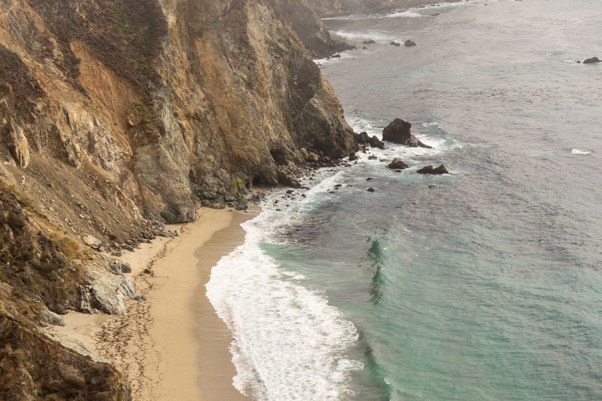 Pacific Coast Highway wrapped in morning fog, golden autumn light catching the cliff edges above the surf