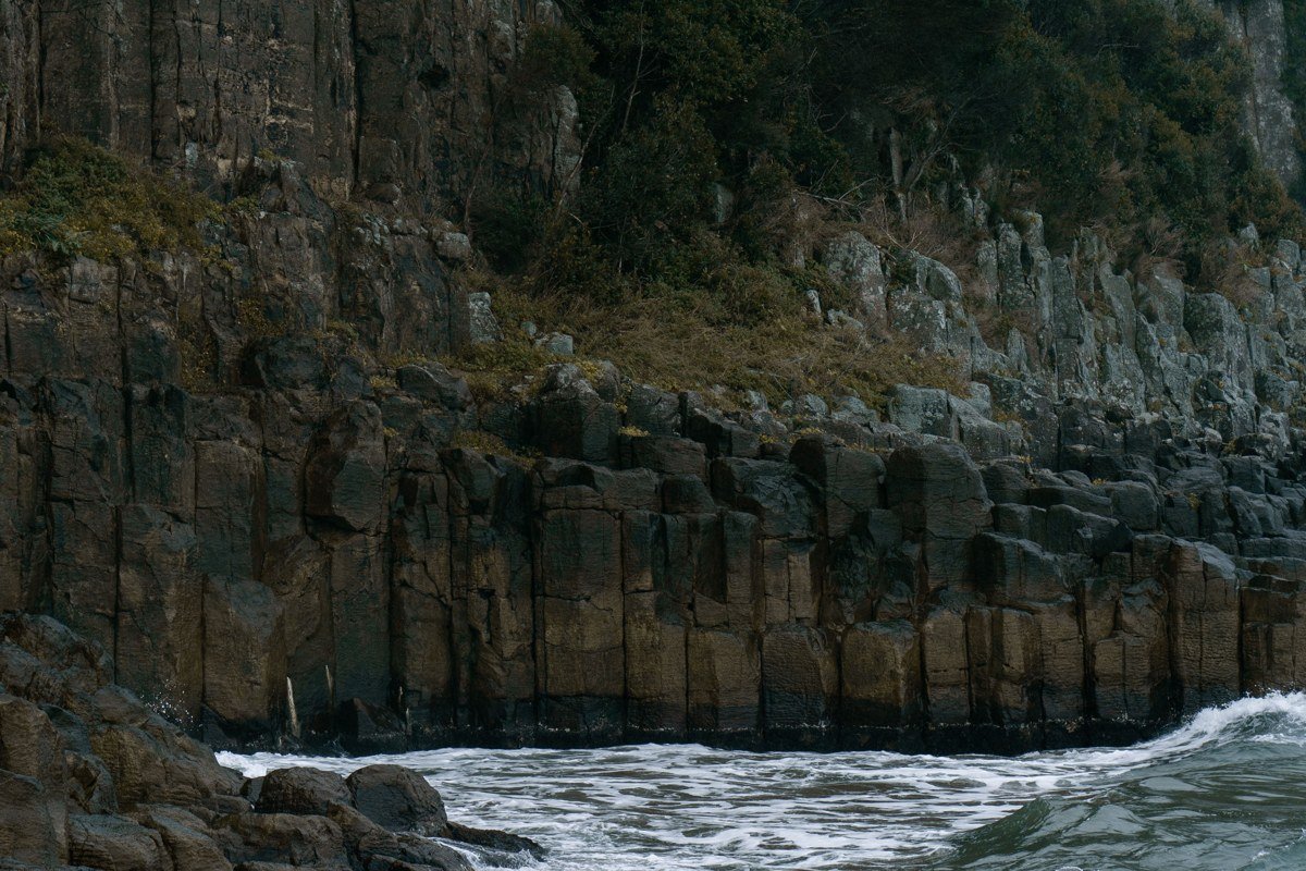 The rocky basalt coast at Yachats, a wave exploding upward through a surge channel, Cape Perpetua's forested headland in the background