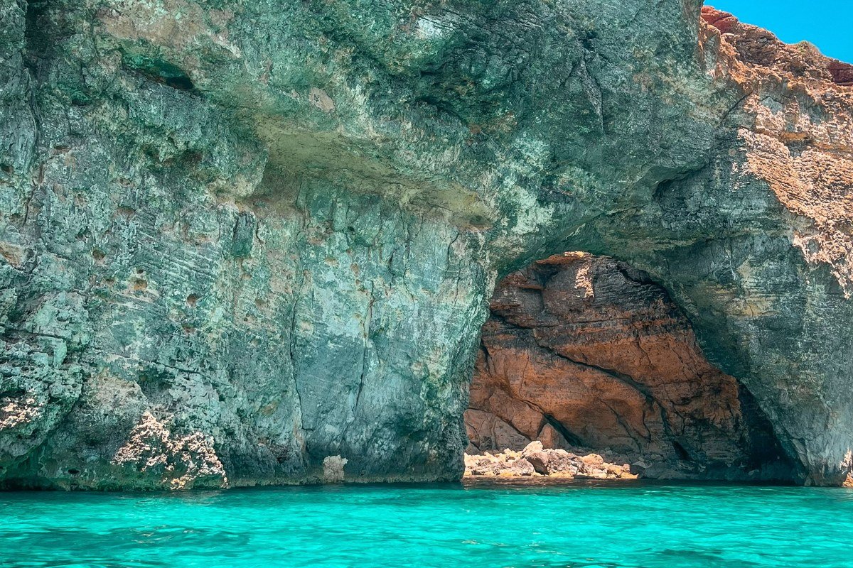 Dwejra Bay, Gozo, late afternoon. The collapsed Azure Window site in the foreground with the Inland Sea tunnel mouth visible to the left. Turquoise water fills the mid-ground. Expose for the limestone to capture its shift from cream to amber in low directional light. No drones without a permit.