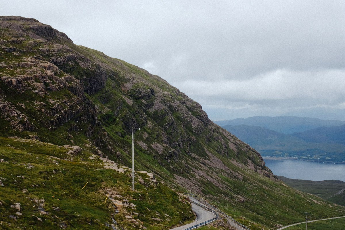 hairpin road climbing through snow-dusted alpine terrain toward coastal panorama, Bealach na Ba Applecross Scotland