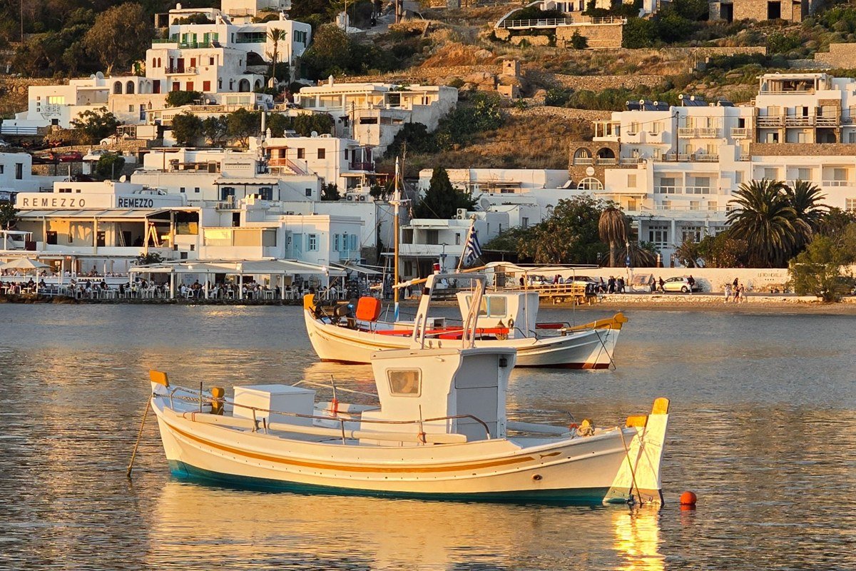 sun-bleached Greek island harbor with colorful fishing boats and whitewashed buildings aerial view