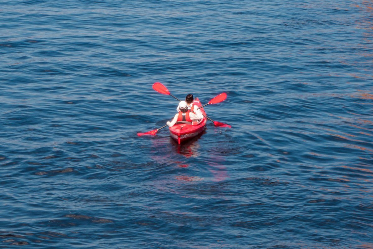 A kayaker in a narrow red boat on the upper Cahabon River, limestone walls green with moss on both sides, the canopy closing so completely above that the light is filtered to a dim aqueous green