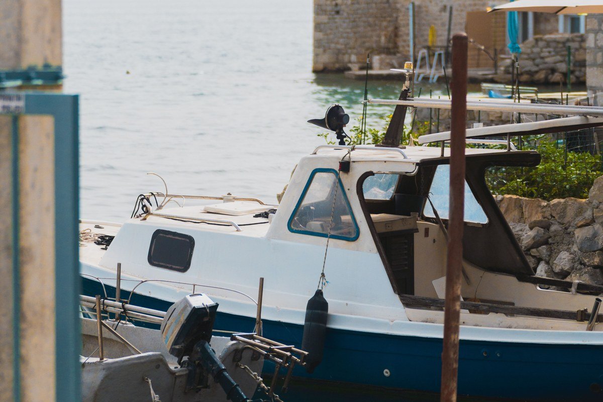 Iraklia village port at dawn, small whitewashed buildings stepping up from waterfront, single fishing boat in still water, Cycladic light raking low across facades, no other vessels visible