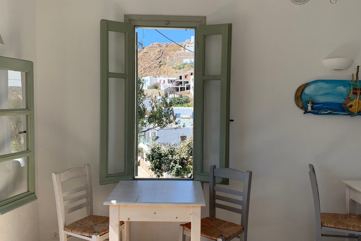 Anafi Chora at midday, stark white cubic buildings against deep blue sky, Kalamos rock monolith visible in far background across open Aegean, shot from above the village looking east, no human figures in frame