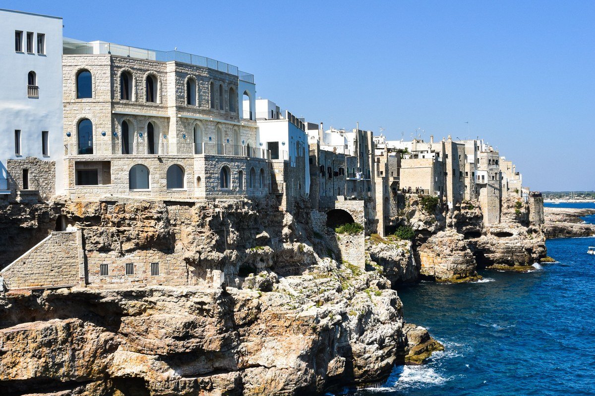 An aerial view of a whitewashed coastal village at golden hour, limestone buildings cascading toward cobalt water with no cruise ships in the frame