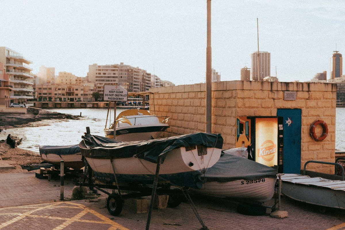 Valletta's honey-limestone harbor at evening, the city's characteristic warm amber glow reflected in the water alongside the painted prows of traditional luzzu fishing boats