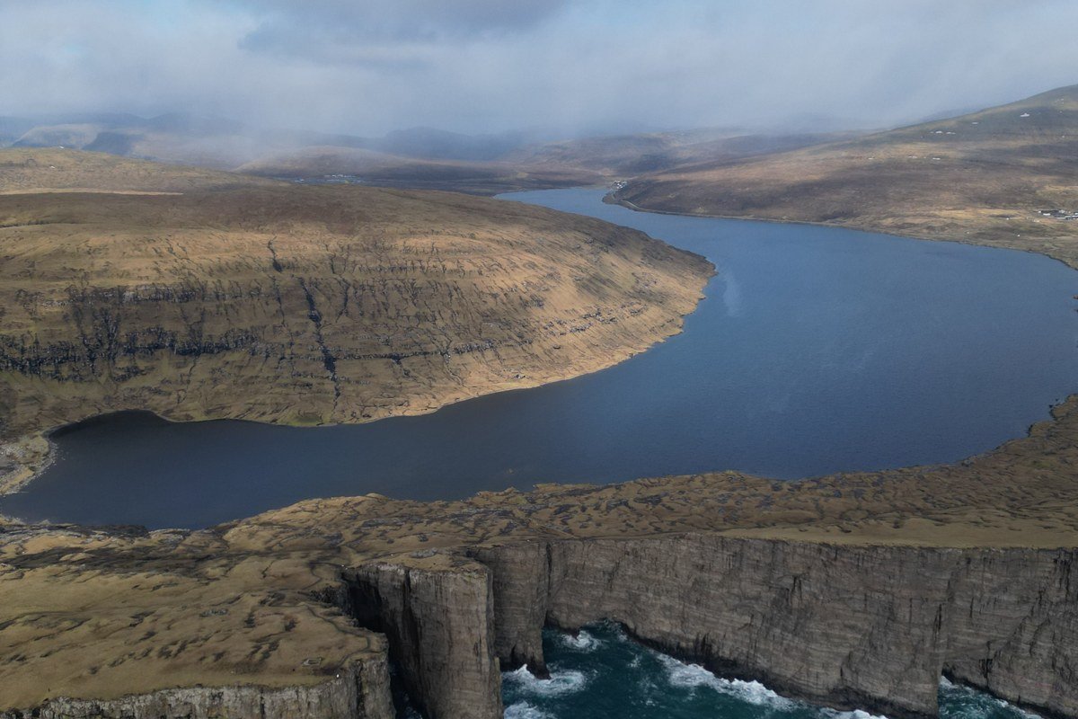 Faroe Islands dramatic sea cliffs with fog and green grass Sørvágsvatn lake aerial view