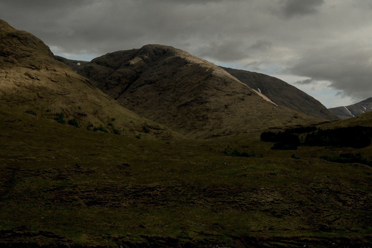 A wide valley in the Scottish Highlands swallowed by low cloud, the moorland saturated dark green and rust-brown, no sky visible above the ridgeline. Shot at 24mm, f/8, the foreground heather sharp while the middle distance dissolves entirely into grey. This is the image most Highlands visitors drive past without stopping. Pin it before you go.