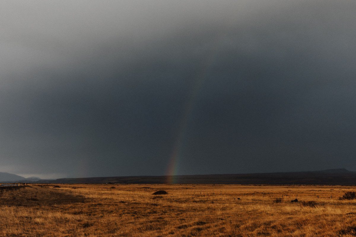 The central monolith at Calanais in moving rain, the stone surface dark and wet, a band of pale light opening briefly between two cloud layers on the western horizon behind it. The surrounding moorland is formless grey-green. No other visitors visible. Shot at 35mm, f/5.6, the monolith filling the left third of the frame and the sky taking everything else. The stones are older than Stonehenge in their current form. In this light, you feel that without needing to be told.