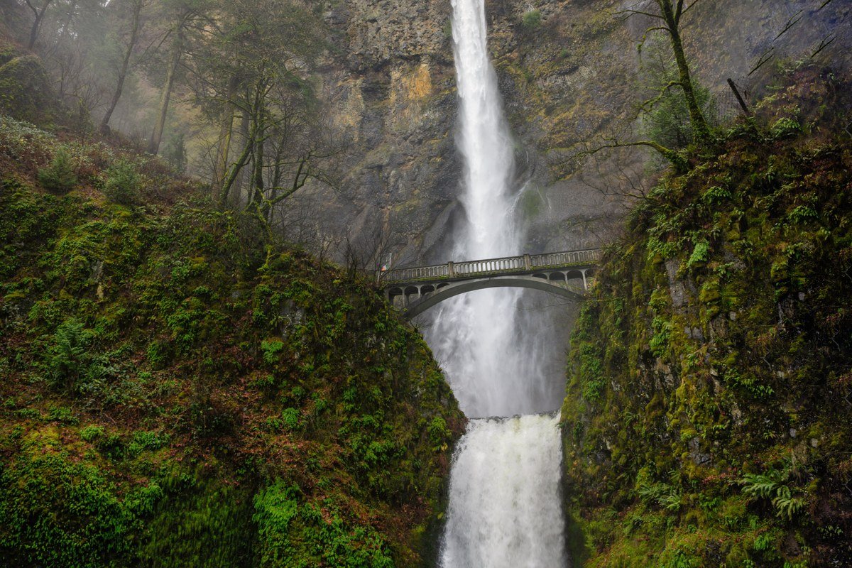Multnomah Falls Oregon with low mist and fog drifting through evergreen canyon walls