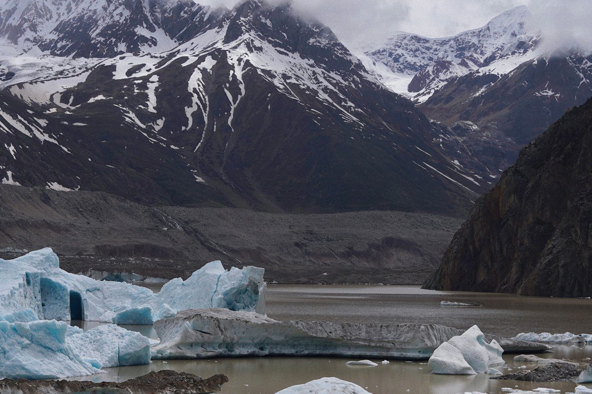 A raft glides between low icebergs on Spencer Lake as the Alaska Railroad glacier-discovery train sits at the platform behind it.