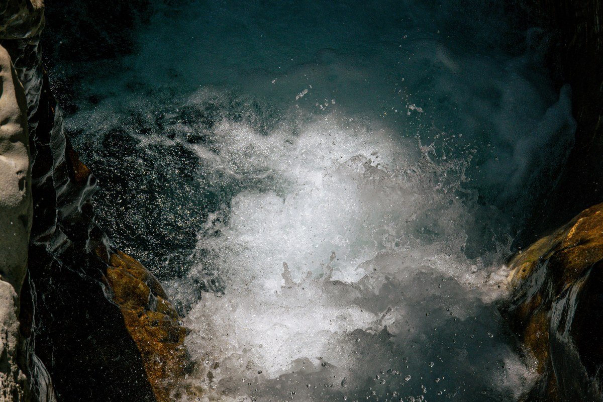 A raft drops through a class III wave train in Keystone Canyon while a waterfall spills down the rock wall directly behind it.