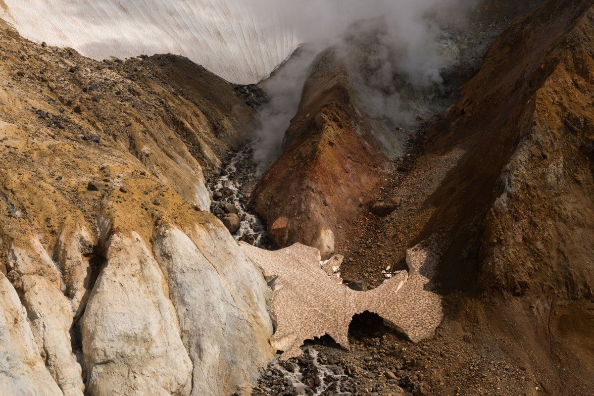 A raft passes below the rust-colored ruins of the Kennecott copper mill as silty glacial water churns past.
