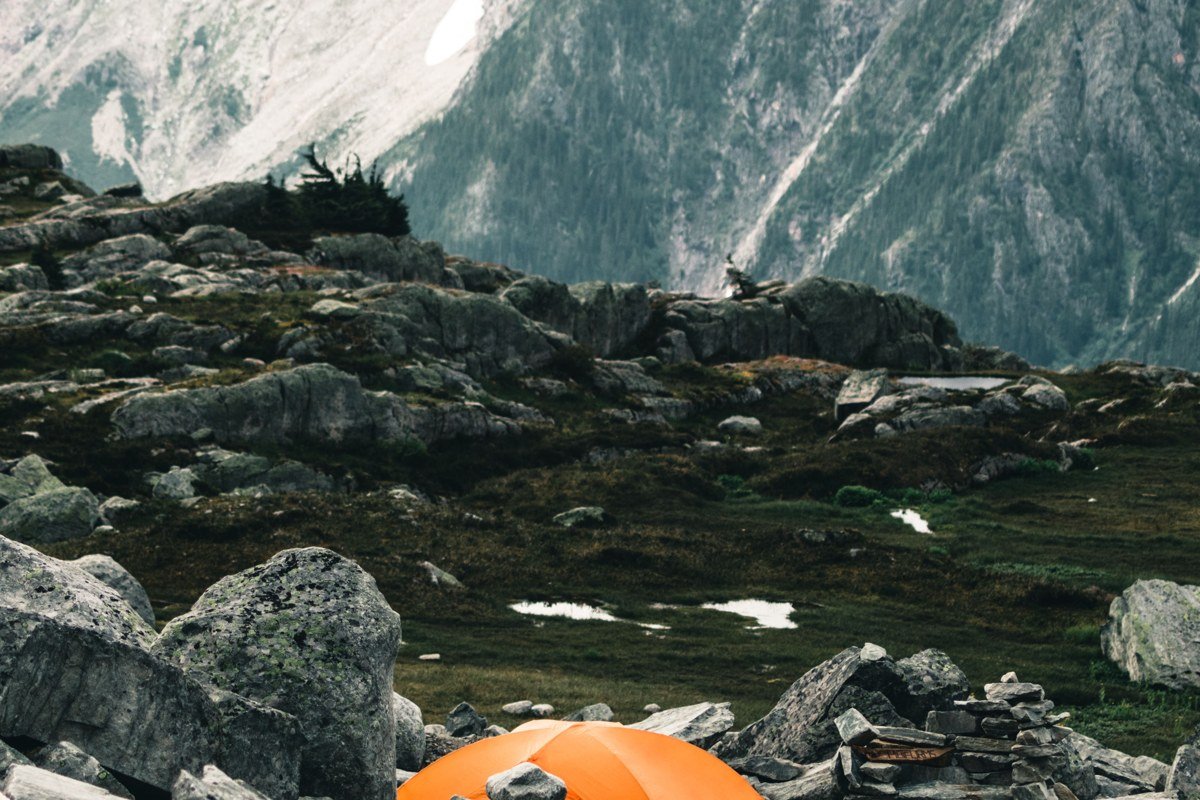 Tents pitched on a gravel bar along the Nizina River, with Wrangell range peaks lit orange at sunset.