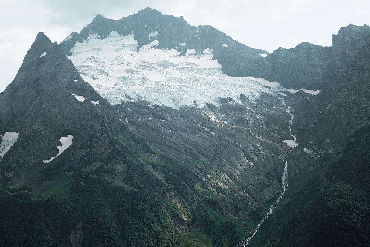 A wide, glacier-fed river braids across a gravel valley floor beneath a heavily crevassed ice field.