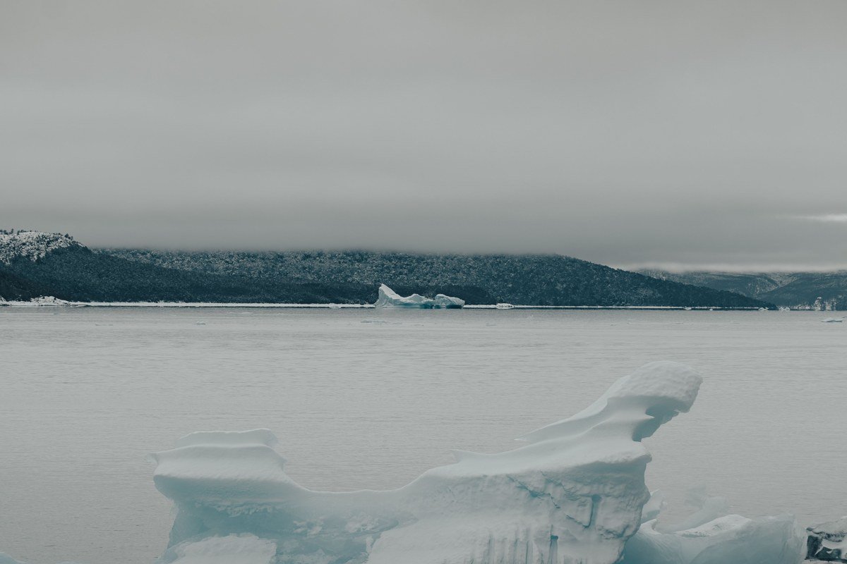 A guided kayak weaves between low, table-sized icebergs on Mendenhall Lake with the glacier's blue face in the distance.