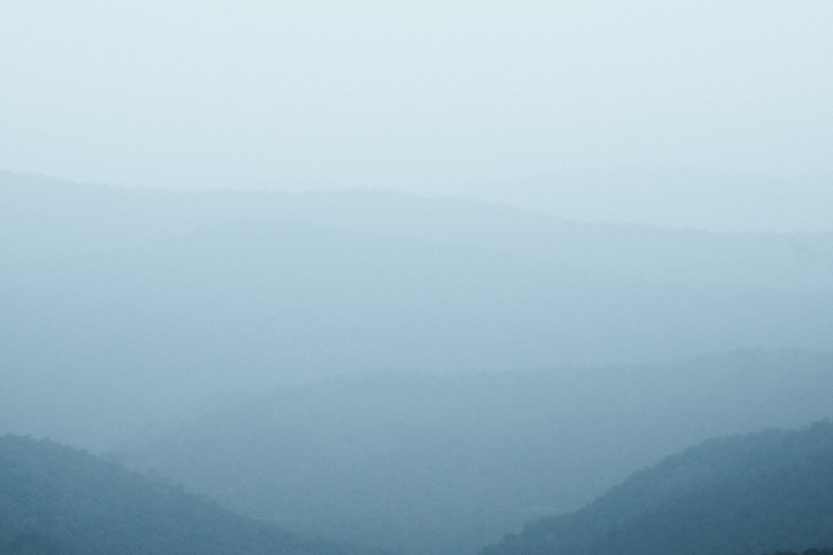 Wide misty Appalachian ridgeline at dawn, layered mountain silhouettes fading into fog, soft golden light