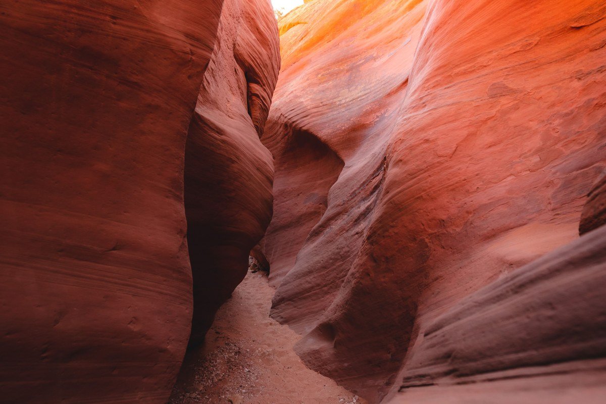 narrow sandstone slot canyon in Zion National Park with a shaft of light hitting orange walls