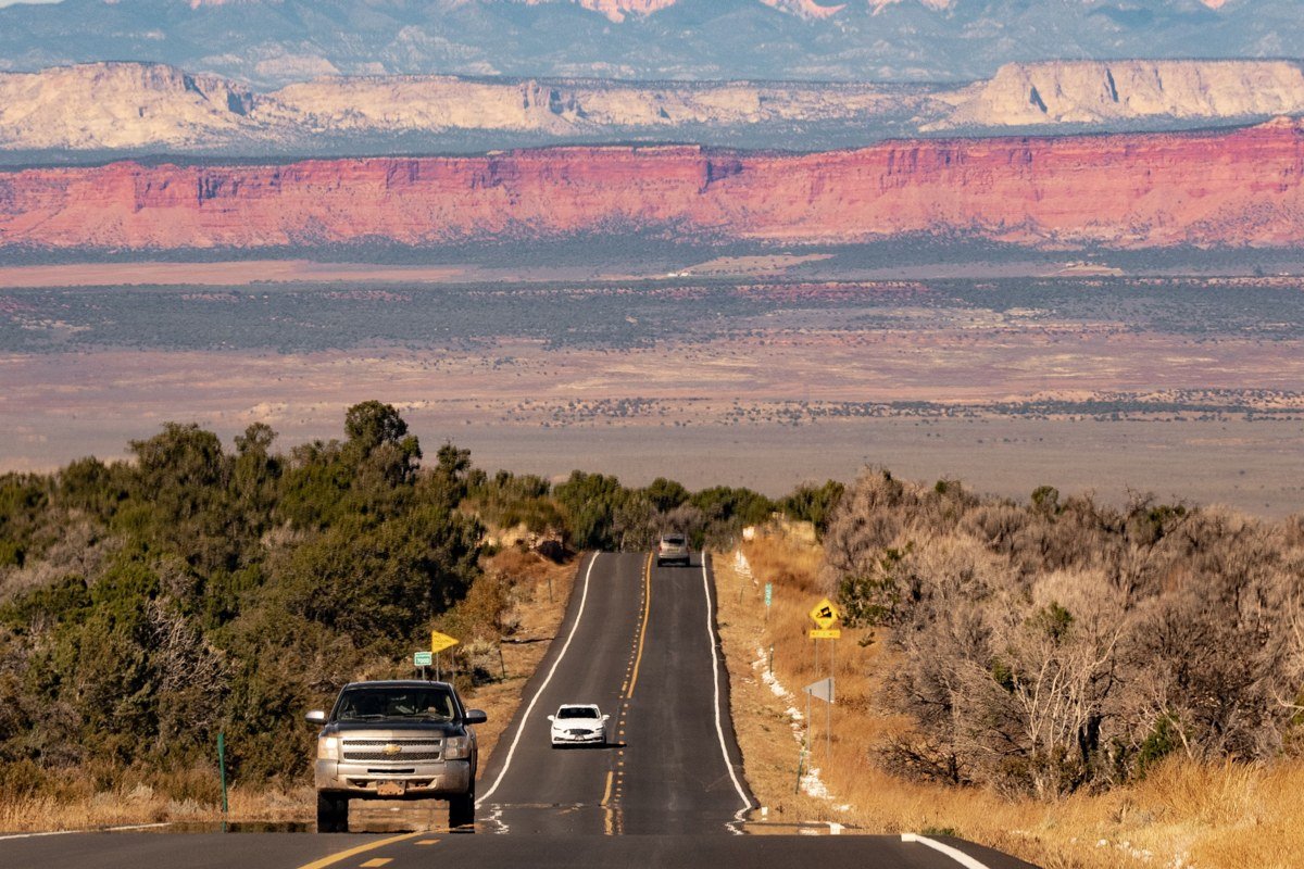 the view east down Highway 24 from the pullout just past the Fruita orchards, mid-afternoon, when the Waterpocket Fold cliffs catch full sun and the road itself is empty in the frame