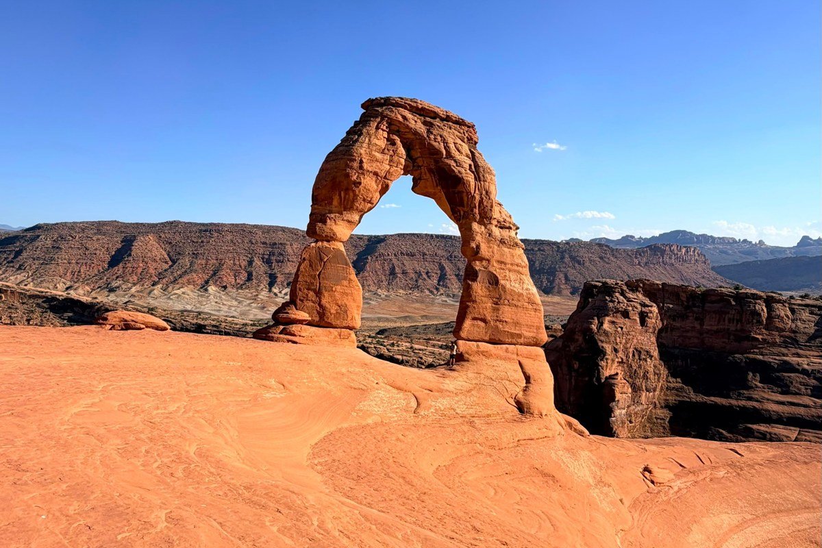 Delicate Arch at last light, shot from the viewpoint across the bowl rather than up close at the arch itself, to include the crowd gathered at the rim for scale