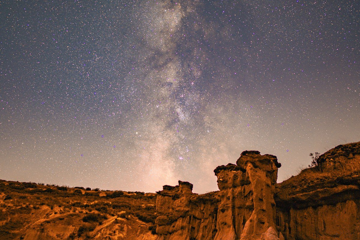 the overlook at Sipapu Bridge in the hour after sunset, long exposure, with the Milky Way visible above the bridge's span