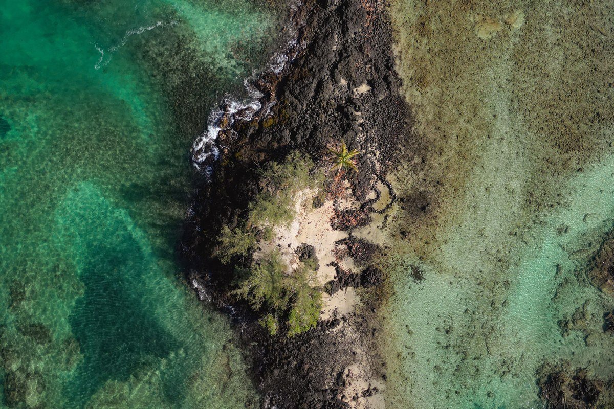 aerial view of a remote Hawaiian coastline with turquoise water, black lava rock, and no buildings in sight